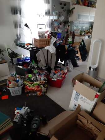 Unaufgeräumtes Wohnzimmer mit Kartons, Hausrat, Spielsachen und Küchenutensilien.