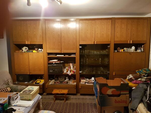 Großer Wohnzimmerschrank aus Holz mit Glastüren, vielen Dekorationsartikeln und Umzugskartons.